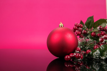 Close up of  red shinning ball decoration and fake green leaves, red cherries on christmas tree isolated in pink background. Eve, Christmas New year concept.