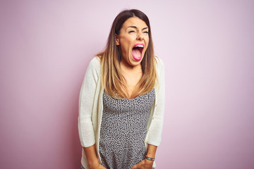 Canvas Print - Young beautiful woman standing over pink isolated background angry and mad screaming frustrated and furious, shouting with anger. Rage and aggressive concept.