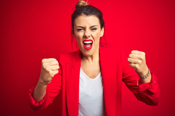 Sticker - Young beautiful business woman standing over red isolated background angry and mad raising fists frustrated and furious while shouting with anger. Rage and aggressive concept.