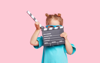 Funny smiling child girl in cinema glasses hold film making clapperboard isolated on pink background. Studio portrait. Childhood lifestyle concept. Copy space for text.