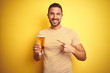 © Krakenimages.com - Young handsome man drinking a pint glass of beer over isolated yellow background very happy pointing with hand and finger