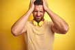 Young handsome man wearing headphones listening to music over yellow isolated background suffering from headache desperate and stressed because pain and migraine. Hands on head.