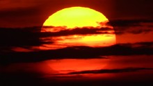Close Up Of A Big Orange And Red Sun Ripping Through Dark Clouds During A Morning Sunrise Over The Ocean.