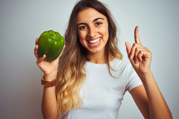 Wall Mural - Young beautiful woman holding green pepper over white isolated background surprised with an idea or question pointing finger with happy face, number one