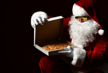 Wall Mural - Santa Claus in sunglasses is opening closing pizza box, looking inside, desiring on black. New year and Xmas fast food