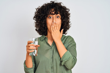 Poster - Young arab woman with curly hair holding glass of water over isolated white background cover mouth with hand shocked with shame for mistake, expression of fear, scared in silence, secret concept