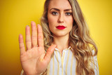 Fototapeta  - Young beautiful woman wearing stripes shirt standing over yellow isolated background with open hand doing stop sign with serious and confident expression, defense gesture