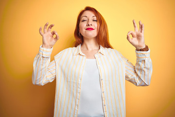 Sticker - Beautiful redhead woman wearing striped shirt standing over isolated yellow background relax and smiling with eyes closed doing meditation gesture with fingers. Yoga concept.