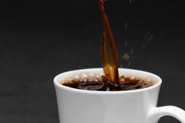 close-up pouring hot black coffee into a white cup, fresh coffee, black background