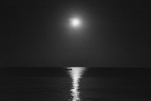 Grayscale Shot Of A Boat In The Calm Sea With The Reflection Of The Moon At Night