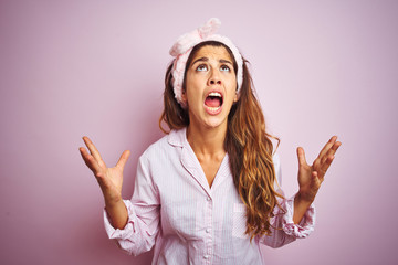 Wall Mural - Young beautiful woman wearing pajama standing over pink isolated background crazy and mad shouting and yelling with aggressive expression and arms raised. Frustration concept.