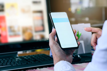 Wall Mural - Cropped shot of man using smartphone while working at office desk, blank screen for graphic design.