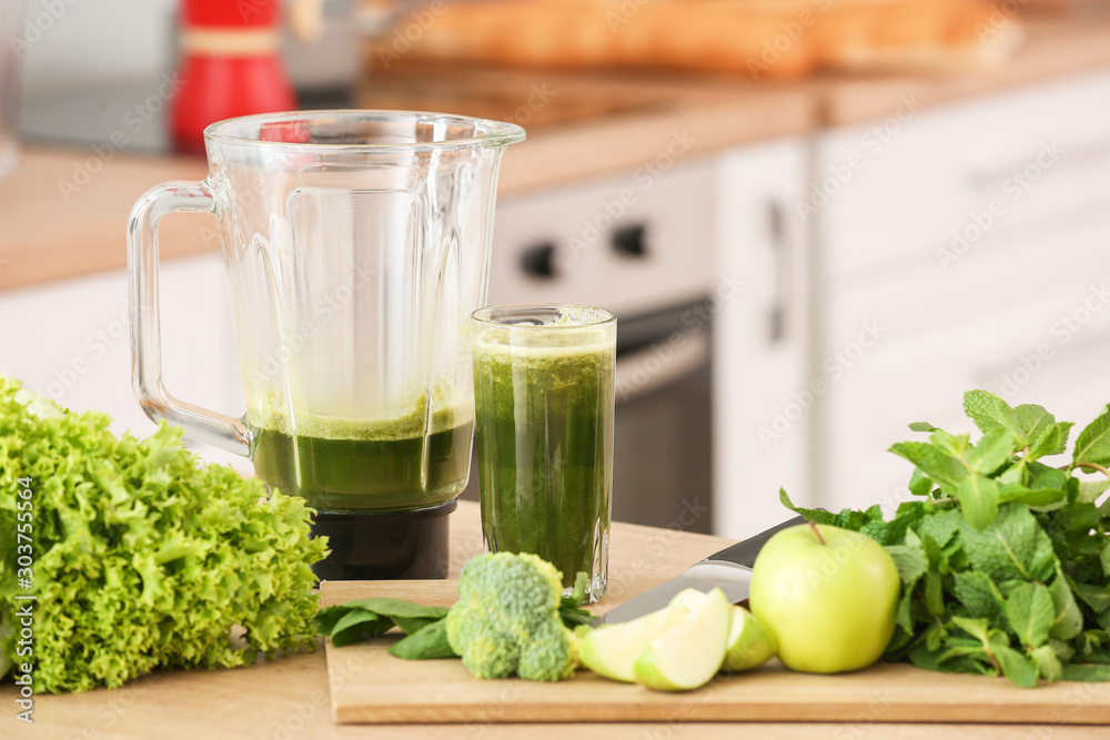 Glass and blender with healthy smoothie and ingredients on table in kitchen