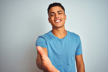 Young Brazilian Man Wearing Blue T-shirt Standing Over Isolated White Background Smiling Friendly Offering Handshake As Greeting And Welcoming. Successful Business.