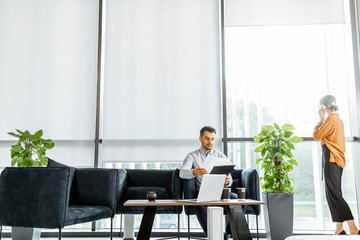 Young couple solving some business or legal affairs at the bank or financial institution office. Wide view with big window and copy space