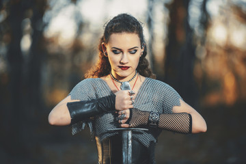 The girl knight in chain mail with a metal sword cosplay in Gothic style. Female warrior Amazon in the forest image for Halloween.