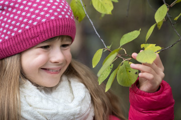 Wall Mural - Pretty child girl wearing warm winter clothes holding tree branch with green leaves in cold weather outdoors.