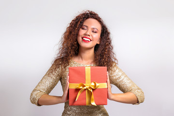 Studio portrait of young woman with dark skin and long curly hair wearing tight sexy dress, holding wrapped present with golden bow. Close up, copy space for text, isolated background.