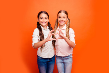 Sticker - Portrait of positive cheerful two kids girl stand together make heart fingers sign of friendly loving family sister relationship wear casual clothing isolated orange color background