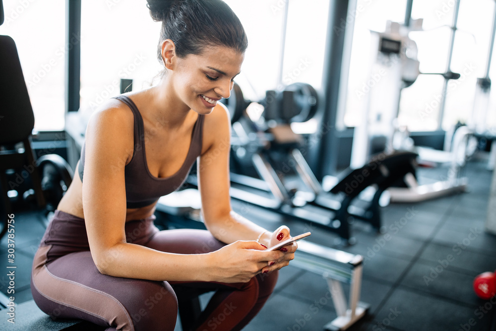 Portrait of sport woman using mobile after exercise at gym. - obrazy, fototapety, plakaty 