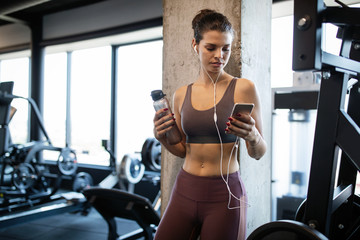 Wall Mural - Young smiling woman at the gym relaxing and listening to music using a mobile phone