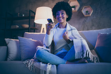 Cheerful Afro American Girl Having Free Time Watch Tv Film Hold Remote Control Switch Channels Sit Divan Crossed Legs Cover Checkered Blanket In Evening Room House Indoors