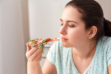 Wall Mural - Breaking Diet. Chubby girl sitting at kitchen table looking at slice of pizza side view lcose-up