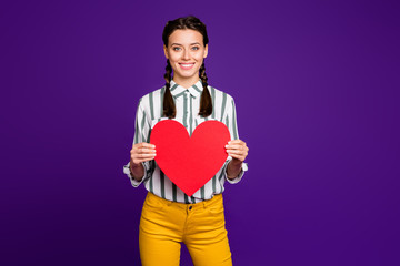 Photo of attractive lady holding big red paper heart celebrating saint valentine day inviting boyfriend on date wear striped shirt yellow trousers isolated purple color background