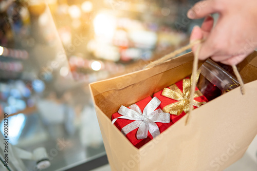 Fotografía Male hand holding paper shopping bag with red gift boxes inside at Christmas event in department store