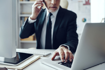 Close up of senior man in elegant business suit talking on the phone while working in modern office