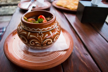 Tasty traditional food meat with vegetables and herbs in a pot on a wooden table.