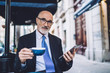 Elderly businessman in glasses with coffee cup and tablet looking at camera
