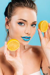 Wall Mural - naked beautiful woman with blue lips holding orange halves isolated on blue