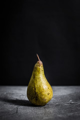 Dark photo of a pear on a stone surface