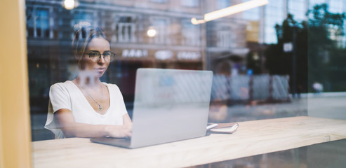 Attractive business freelancer typing text message about future event for distance workers using good internet connection on laptop computer, young female student chatting with friends online