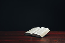 Open Bible On A  Red Wooden Table. Beautiful Black Background.