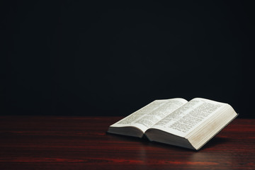 Aufkleber - Open bible on a  red wooden table. Beautiful black background.