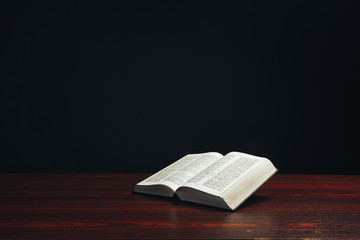 Aufkleber - Open bible on a  red wooden table. Beautiful black background.