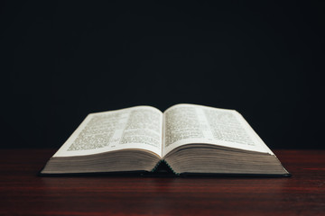Aufkleber - Open bible on a  red wooden table. Beautiful black background.