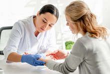 Attractive Dermatologist In White Coat Examining Skin Of Patient In Clinic
