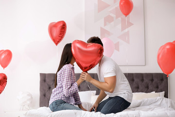 Wall Mural - Romantic couple hiding behind heart shaped balloon in bedroom. Valentine's day celebration