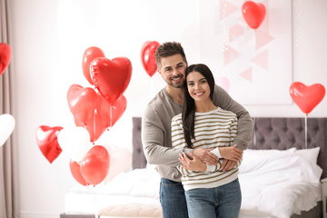 Poster - Lovely young couple in bedroom decorated with heart shaped balloons. Valentine's day celebration