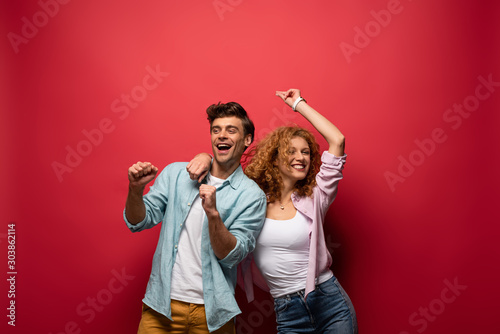 Fotografía beautiful excited couple dancing in casual clothes isolated on red