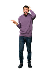 Wall Mural - Full-length shot of Handsome man with sweatshirt surprised and pointing finger to the side over isolated white background