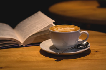 Ceramic cup of cappuccino in coffee shop with pattern on a wooden table with an open book. Latte art. Morning drink. Caffeine.