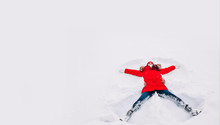 Happy Young Woman In Red Lying On Snow And Making Snow Angel Figure With Hands And Legs
