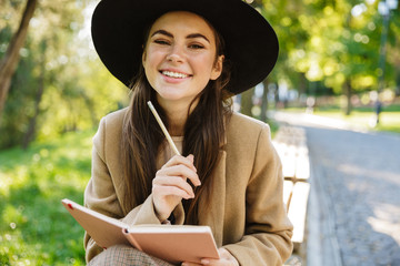 Sticker - Image of caucasian woman holding diary book while sitting on bench in park