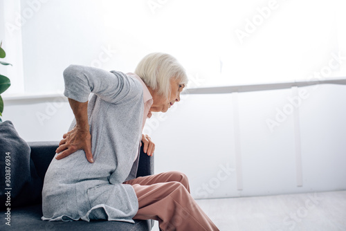 Fotografía side view of senior woman having back pain in apartment