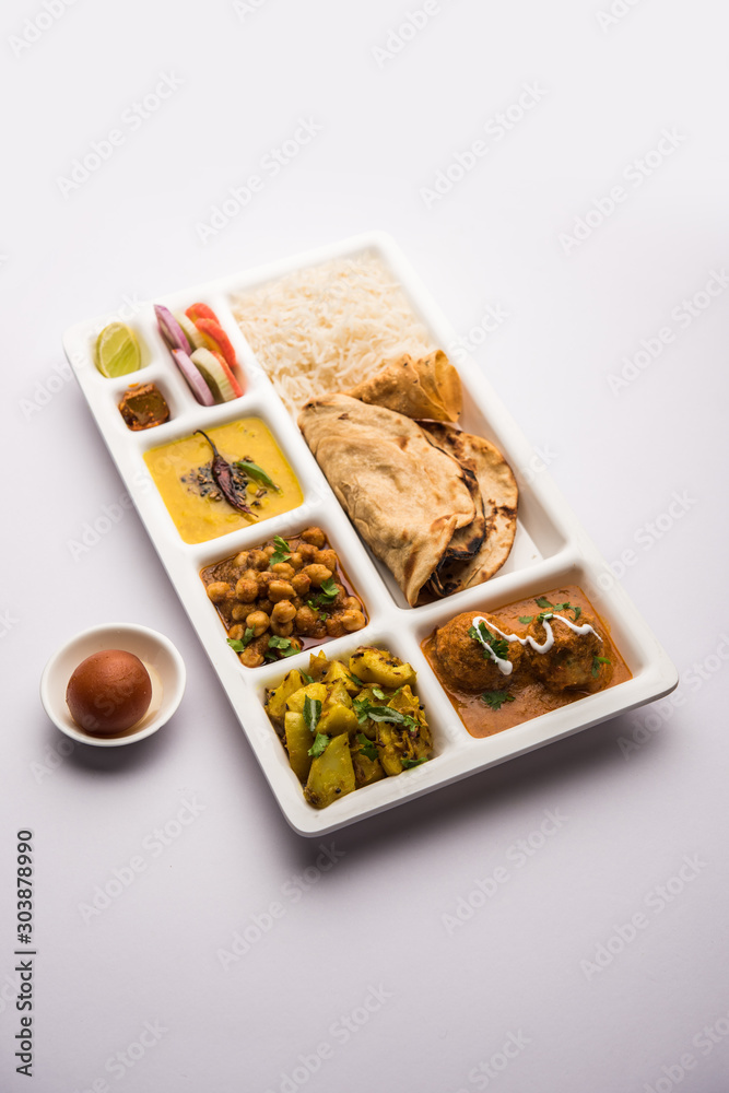 Indian vegetarian Food Thali or Parcel food-tray with compartments in which Malai Kofta, chole, Dal tarka, dry aloo sabji, chapati and rice with sweet gulab jamun served