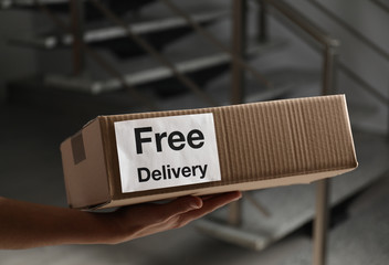 Canvas Print - Courier holding parcel with sticker Free Delivery indoors, closeup